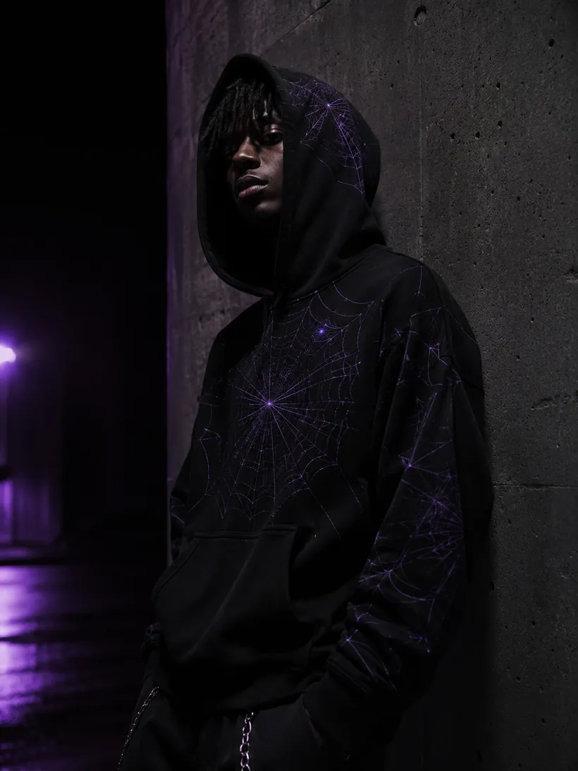 Model with the hood up in a black Spider web-print hoodie